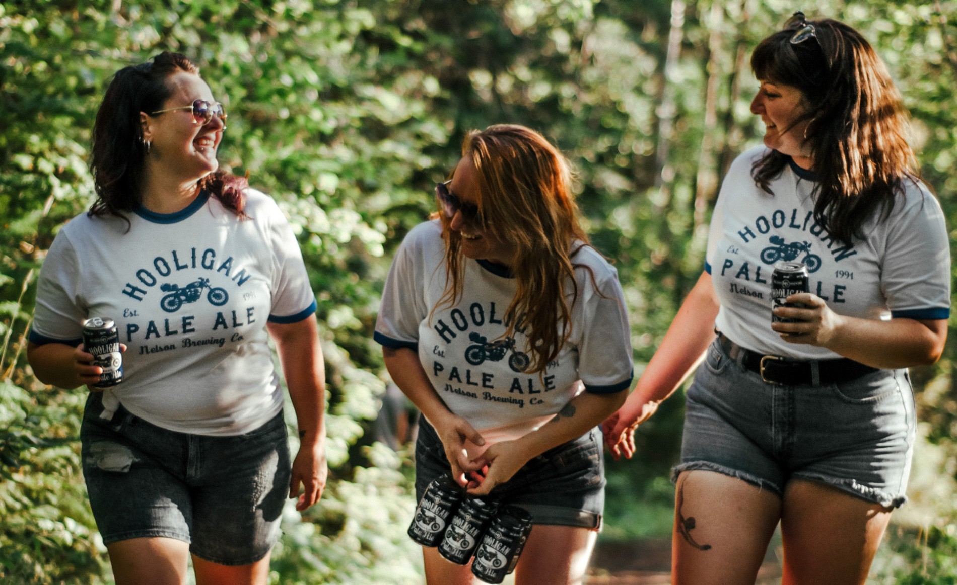 Three woman walking a trail holding Hooligan Pale Ale